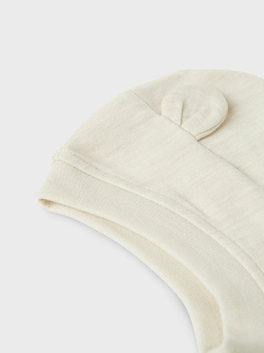 Söt beige balaclava till din baby pojke eller flicka. Mysig mössa som sitter bra på din bebis huvud och du vet att det inte blir kallt i nacke, hals och att endast babyns lilla ansikte sticker fram ur den varma mössan. Ull är ett naturmaterial känt för sina termiska egenskaper, mjukhet och fluffiga utseende. I kallt väder håller ull värmen och under varma dagar absorberar den svett, vilket gör den till ett bra val oavsett årstid.