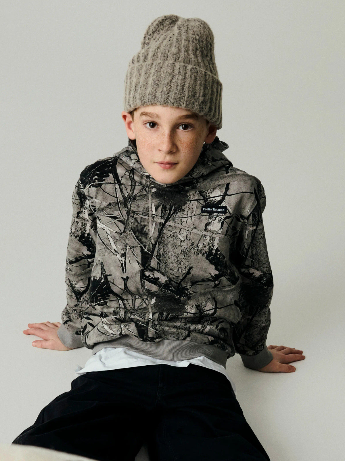 Name It Rasse gråsvart hoodie för pojke med heltäckande skogsmönster och huva.