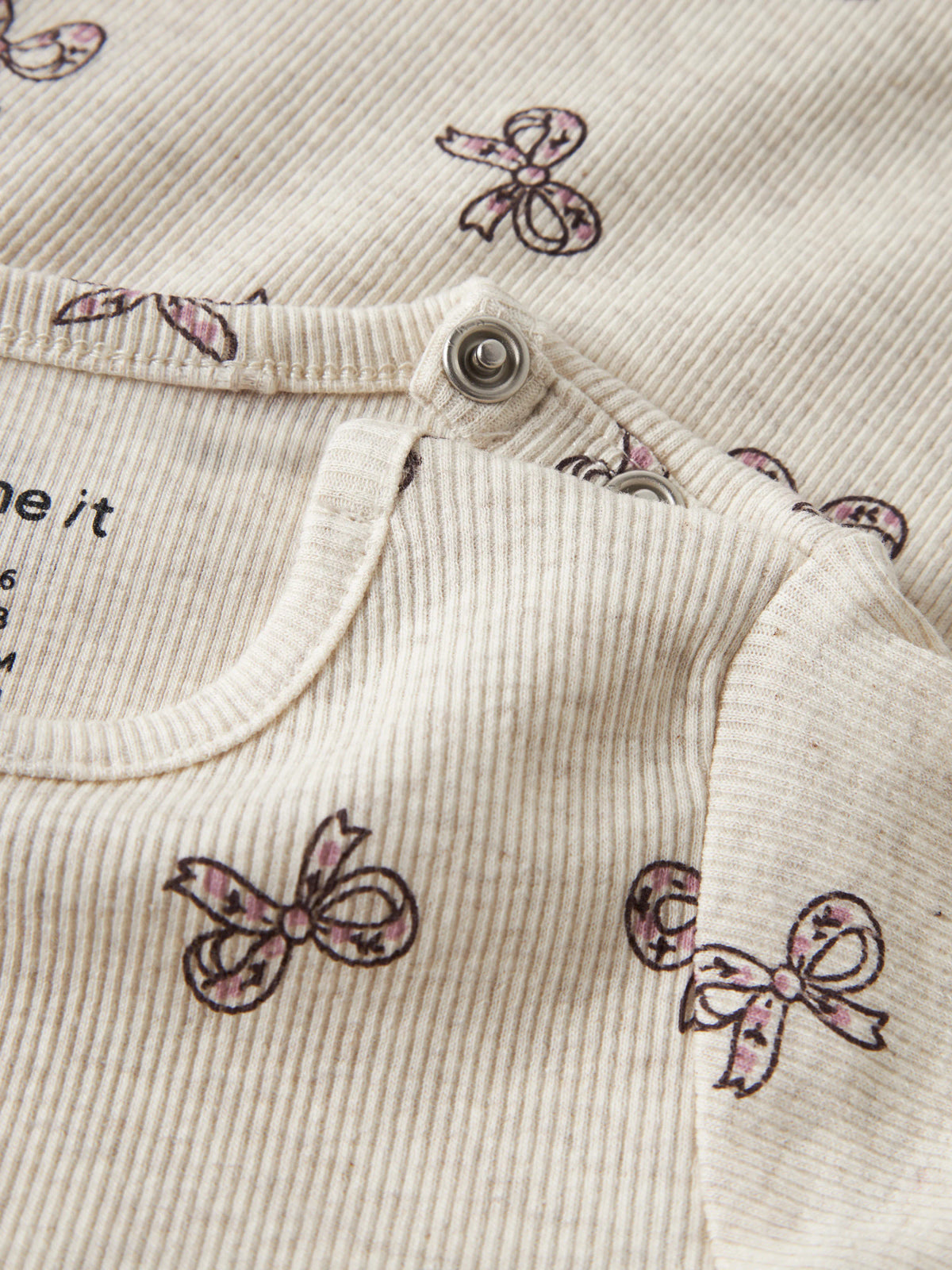 Rulies långärmad ribbad babybody för flicka från Name It i ljusbeige med små rosa rosetter och tryckknappar i grenen.