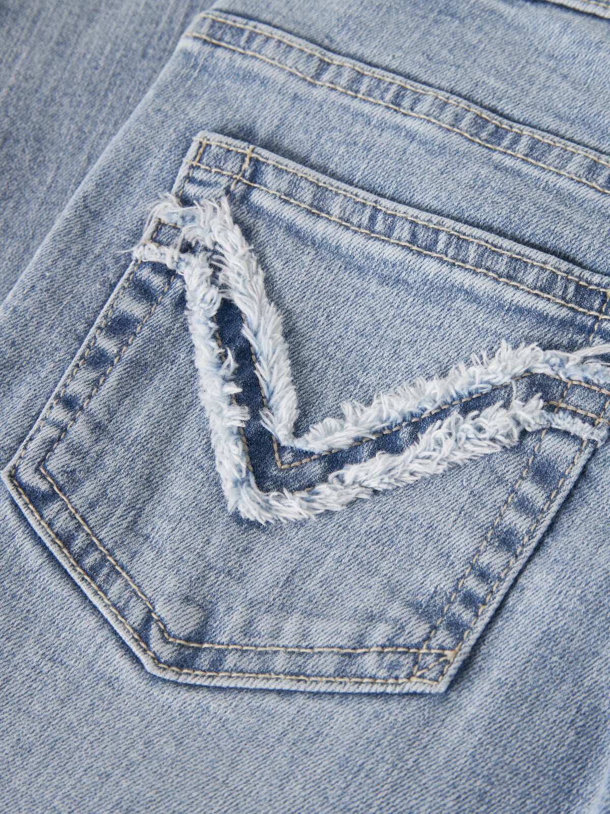 Närbild på fransig V-formad detalj på bakfickan på Polly jeans