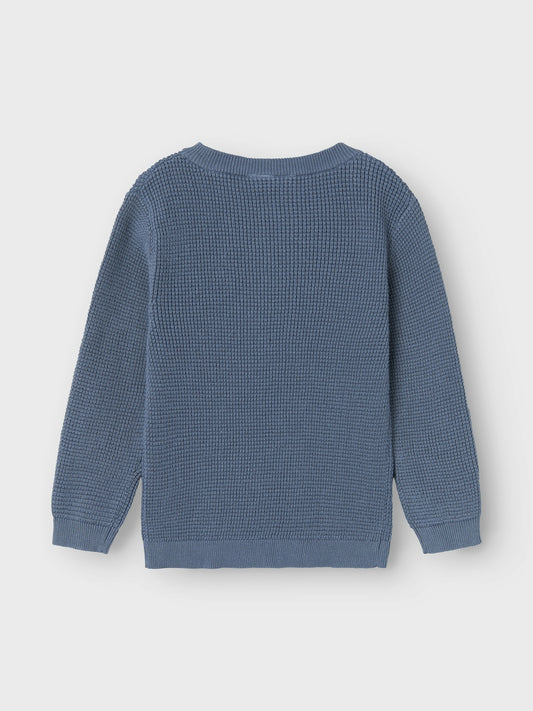 Blå stickad ekologisk tröja med knappar i hals till liten kille, pojke. 
Sätt ihop den perfekta outfiten för ditt barn med kvalitativa vardagsstilar och skapa en bekväm och trendig look. Våffelstickning kännetecknas av sin distinkta yta med små rektanglar för en cool textur.

Detaljtyp: Stickad tröja
Hals: O-hals
Ärm: Långa ärmar (L/S)
Muddar: Ribbstickade muddar
Stängning: Knäppning
Passform: Normal passform