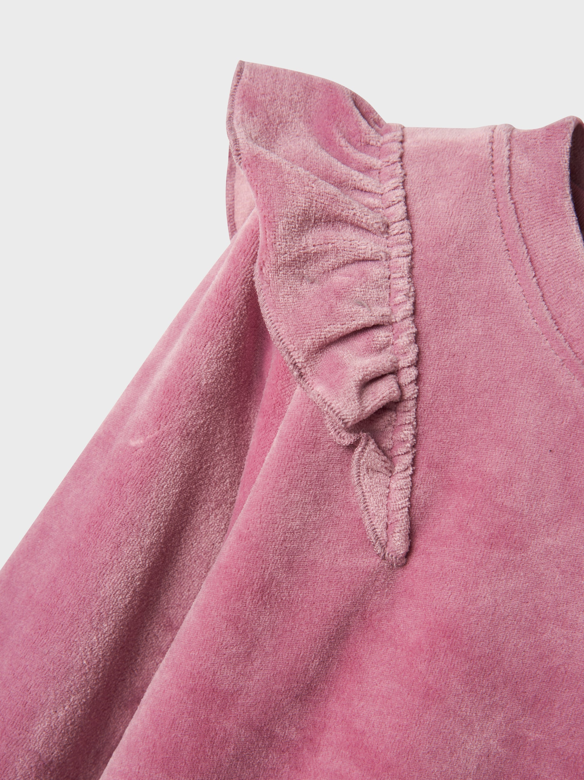 Rosa mysig velour tröja till barn med volanger på axlarna. Låt din flicka få en söt mjuk tröja i återvunnen polyester. 
Välkommen bekväma och coola sweatshirts till ditt barns garderob och skapa en trendig och avslappnad look. Velour är ett mjukt och glänsande tyg med fibrer som följer handens drag för en fin effekt.

Produkttyp: Sweatshirts
Hals: Rund hals
Ärm: Lång ärm
Muddar: Ribbstickade muddar
Passform: Normal passform