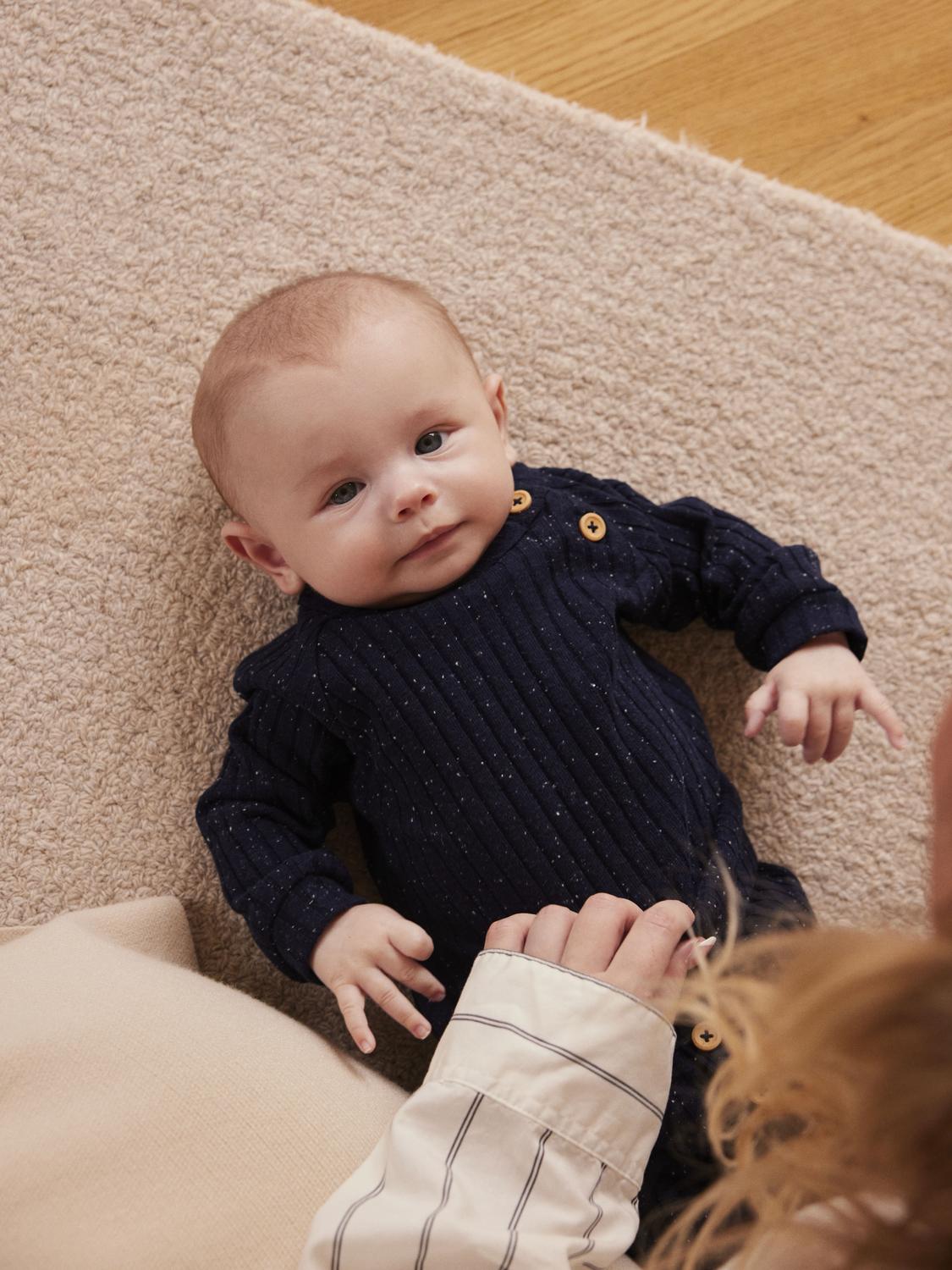 Baby klädd i blå tröja med lång ärm, knappar på ena axeln för enkel av och på klädnad. Tillverkad av ekologisk bomull. Skön tröja till din lilla bebis.