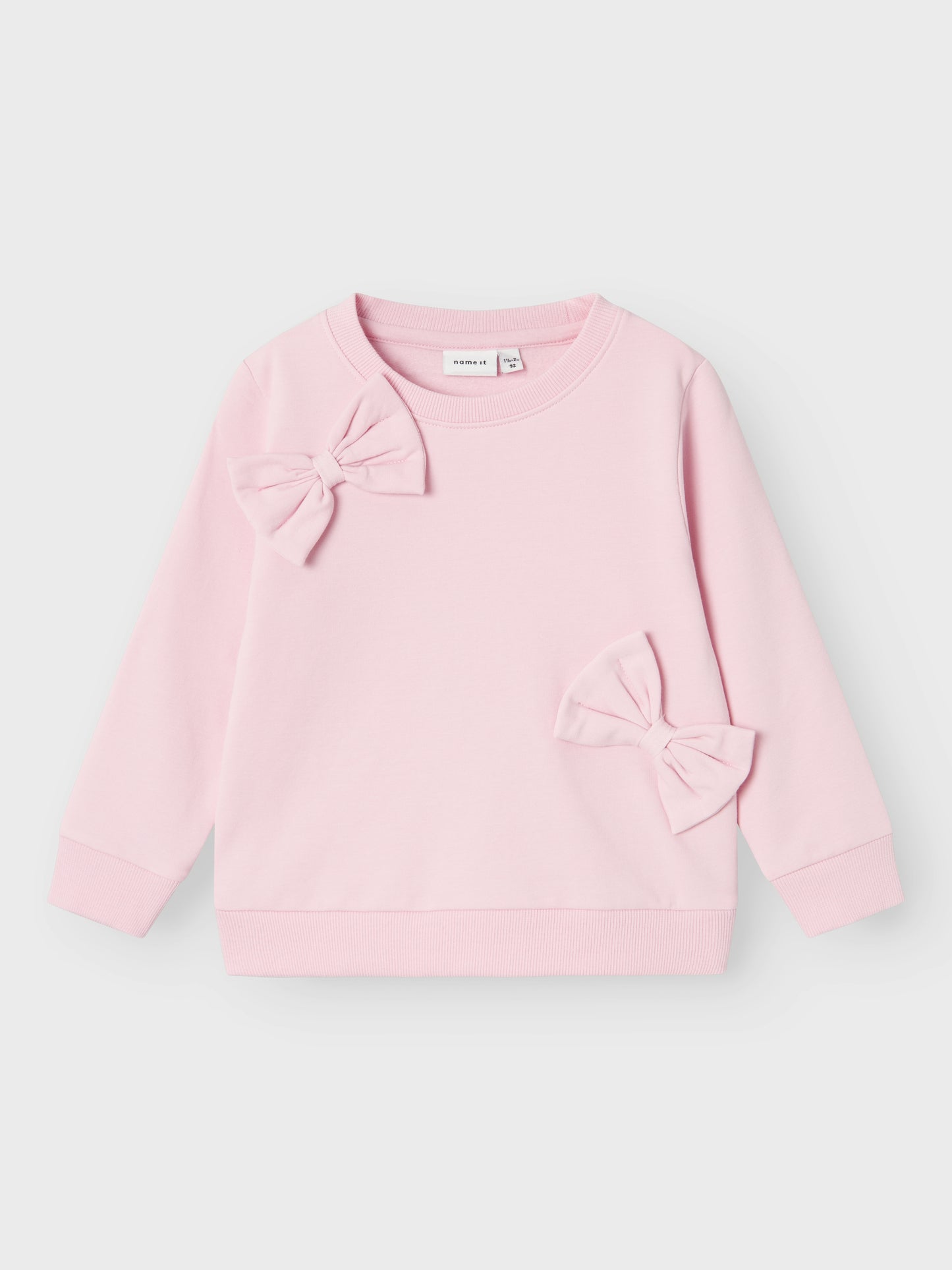 Söt enfärgad rosa sweatshirt tröja med stora rosetter till flicka, tjej.
Välkommen bekväma och coola sweatshirts till ditt barns garderob och skapa en trendig och avslappnad look. Borstad sweatshirt i ekologisk bomull har en mjuk insida för en bekväm känsla till ditt barn.

Produkttyp: Sweatshirts
Hals: Rund hals
Ärm: Långa ärmar
Muddar: Ribbstickade muddar
Extra detaljer : Bowdetalj, 3D-detalj
Passform: Normal passform