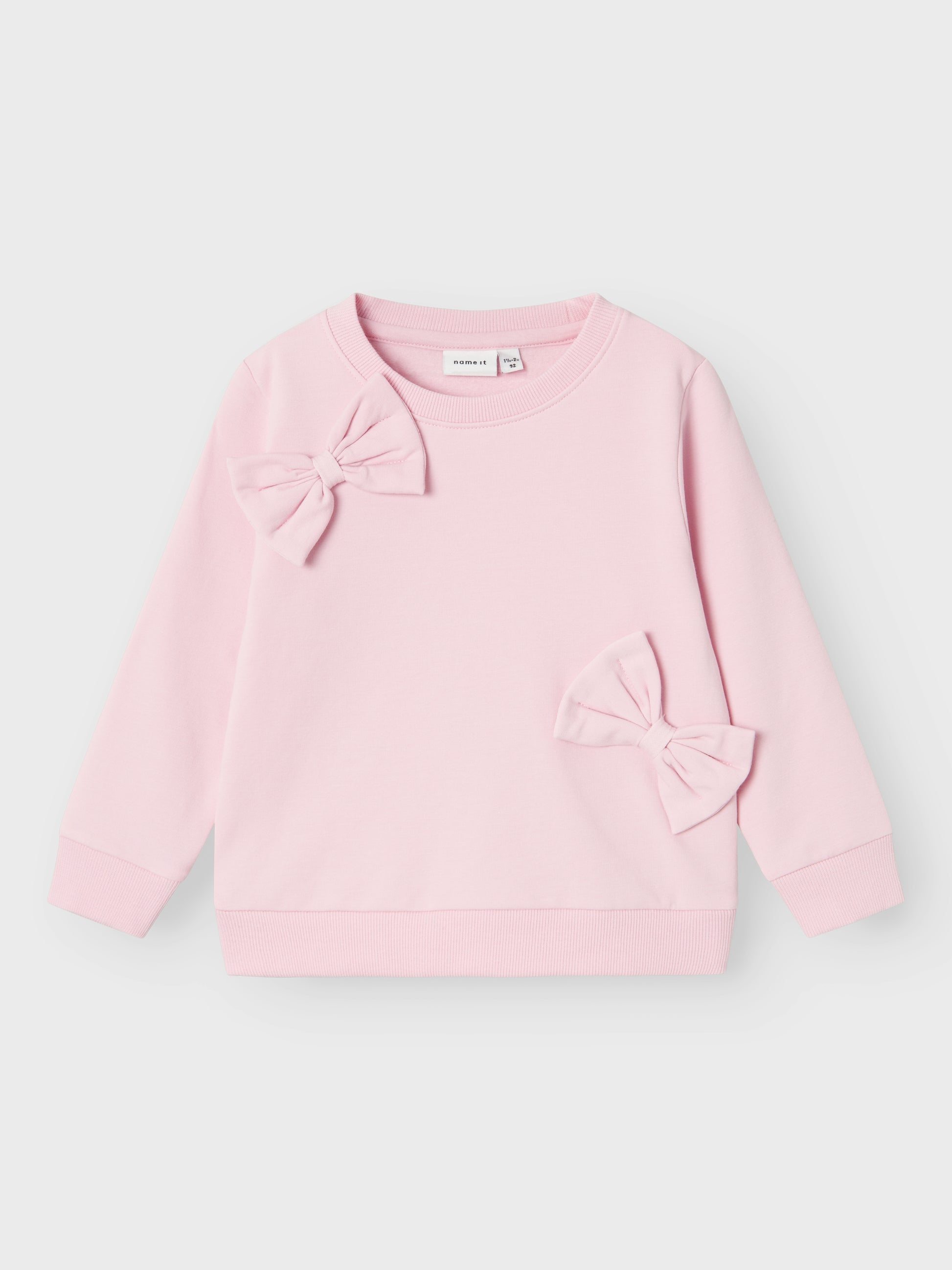 Söt enfärgad rosa sweatshirt tröja med stora rosetter till flicka, tjej.
Välkommen bekväma och coola sweatshirts till ditt barns garderob och skapa en trendig och avslappnad look. Borstad sweatshirt i ekologisk bomull har en mjuk insida för en bekväm känsla till ditt barn.

Produkttyp: Sweatshirts
Hals: Rund hals
Ärm: Långa ärmar
Muddar: Ribbstickade muddar
Extra detaljer : Bowdetalj, 3D-detalj
Passform: Normal passform