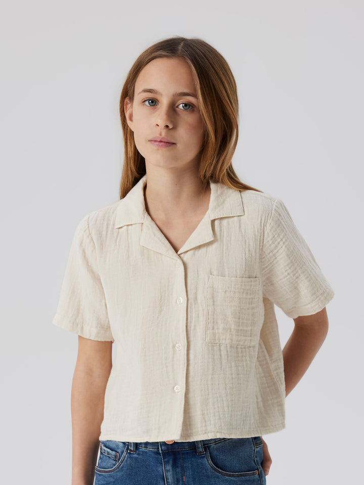 Tjej klädd i kortämad beige blus, skjorta i sval och skön muslin till. Barn topp till flicka från Name it.
NKFJASMIN SS SHORT SHIRT NOOS
13240427